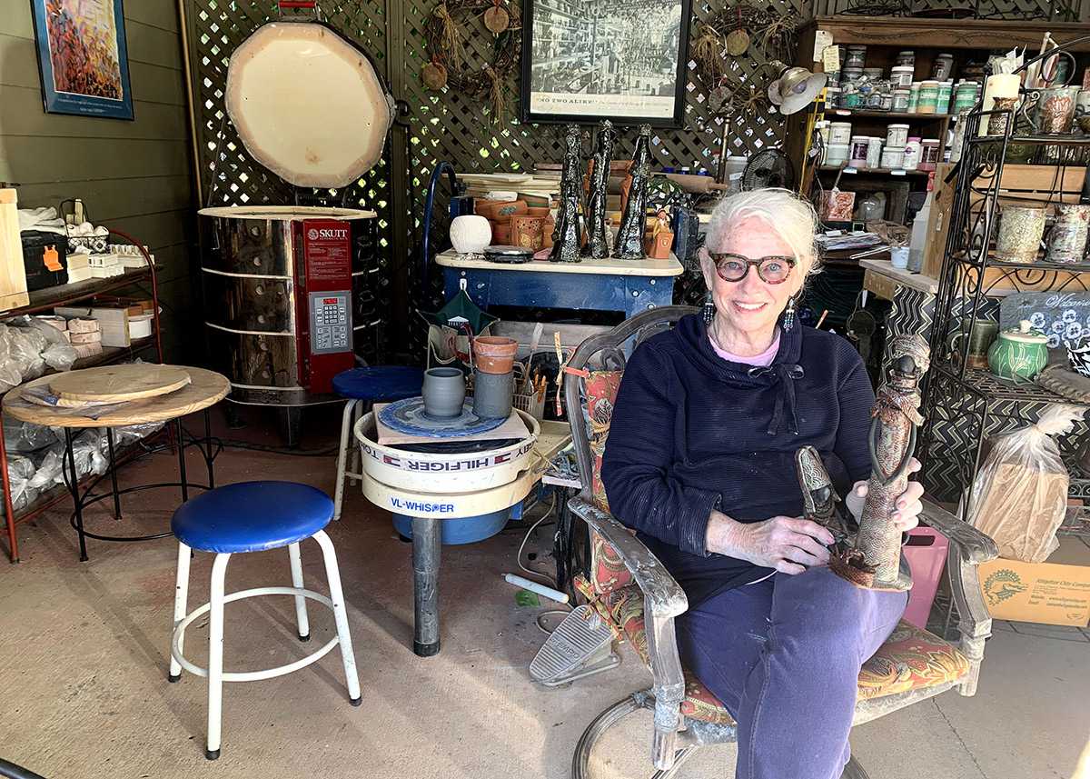Lillian Bridwell-Bowles sitting in her garage holding a scultpure from her Okra Goddess collection