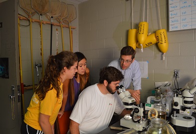 Professor Kaller showing students an object through microscope.