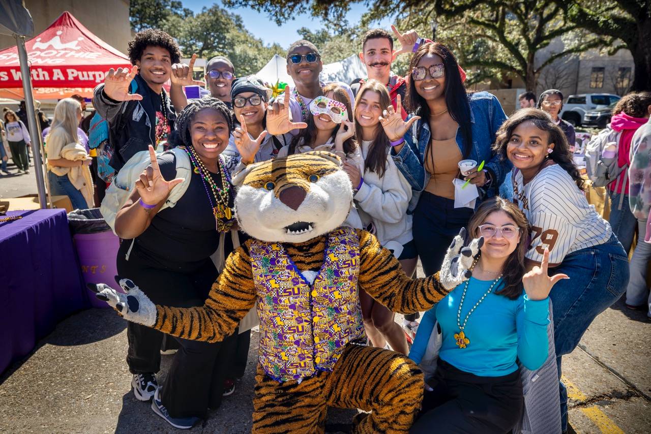 Mike mascot dressed in colorful attire poses with students