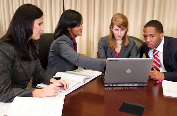 An older photo of CIA alumni talking and pointing at a computer screen, everyone is in business attire