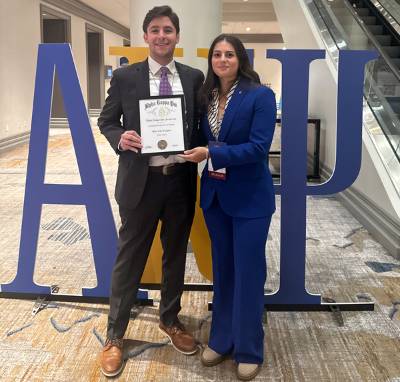 Two LSU students stand in front of the letters AKPSI and hold a certificate