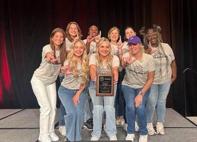 LSU Beta Alpha Psi members gather for a group photo on a stage in Orlando. They hold an award plaque as they smile at the camera.