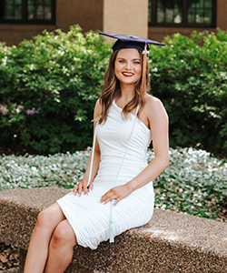 Photo of Jordan wearing a white dress and sitting in the Courtyard on campus