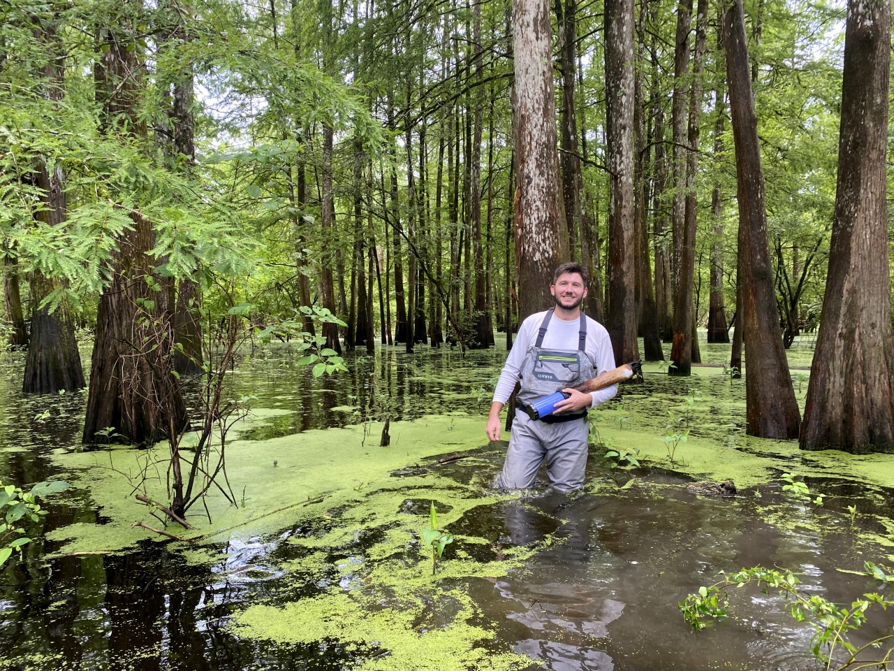 a man in waders stands in thigh-migh marsh water