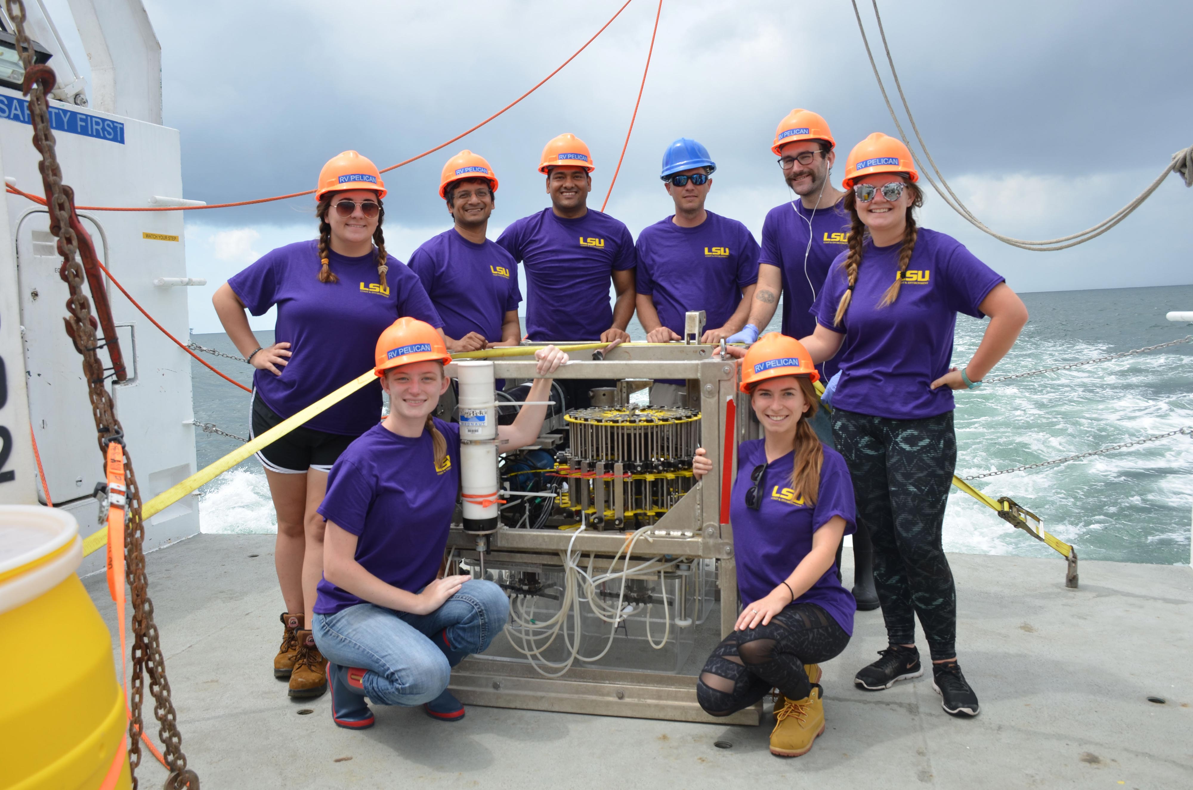 a group of people in matching shirts and helmets pose with scientific equipment on a ship