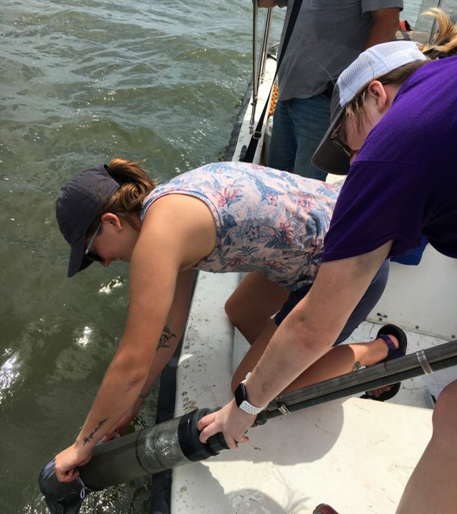 Researchers reach over the side of a boat to retreive a core sample