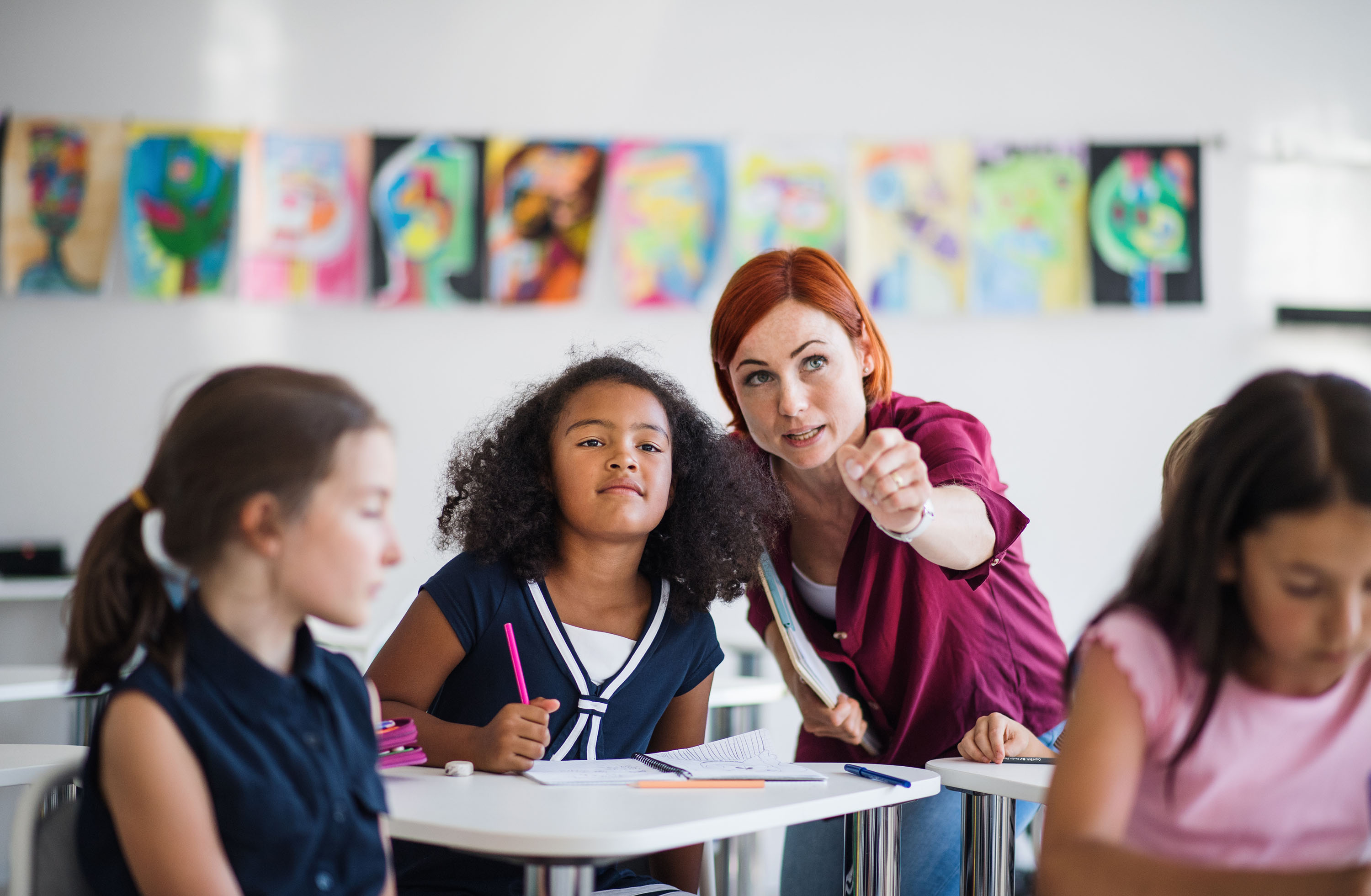 teacher with red hair assisting black girl in an elementary classroom