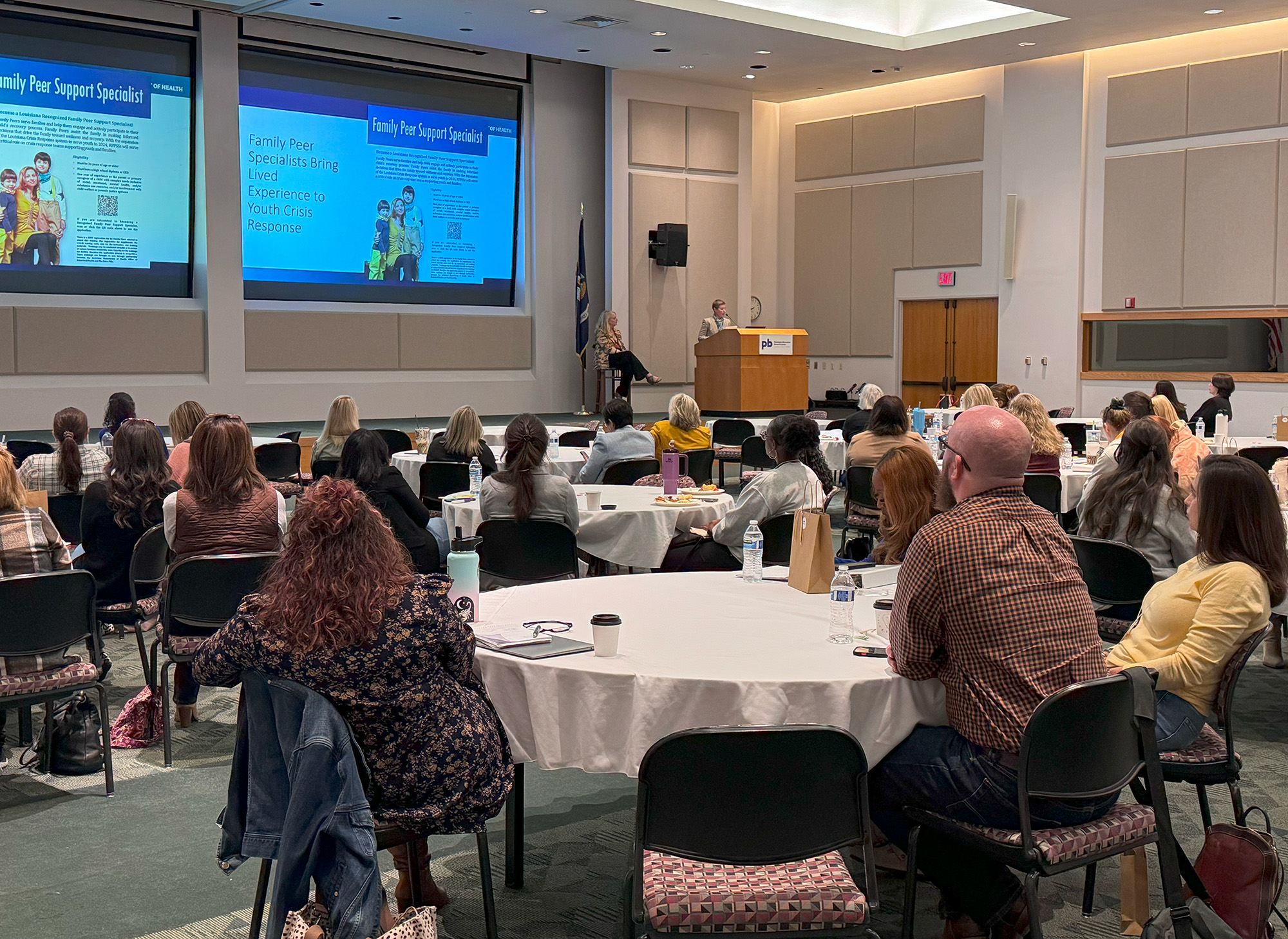 presentation at conference with audience at round tables facing speakers on stage