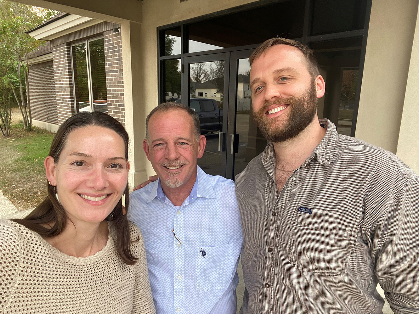 Anne Thomas, Bryan King, and Joshua Wartelle smiling outside a building