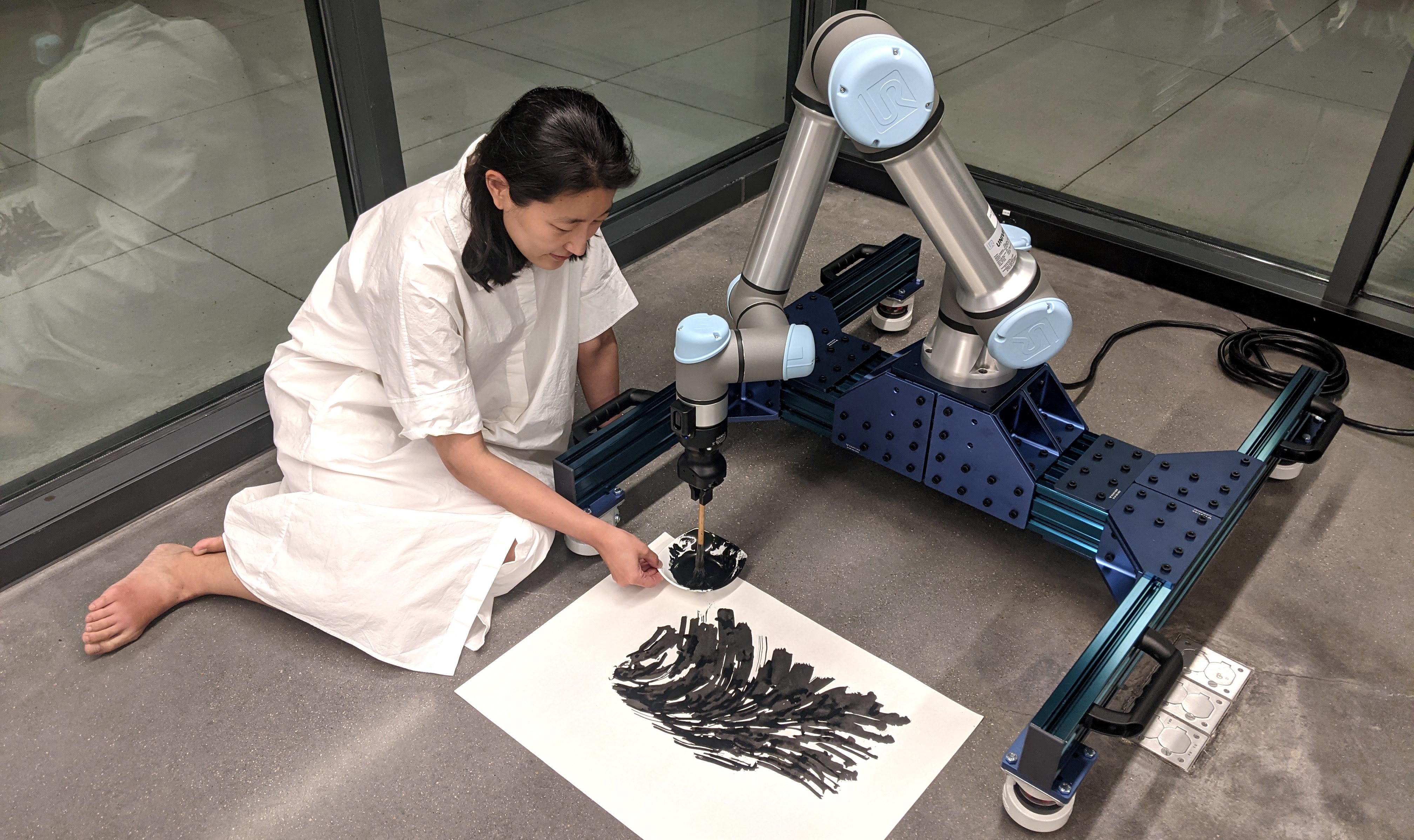 一个拿着画笔的机器人和一个坐在地板上拿着一碗颜料的女人