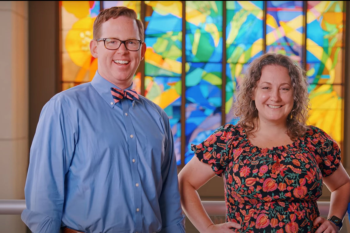 Dr. Vance L. Albaugh and Dr. Amelia Jernigan pose in front of a stained-glass window.