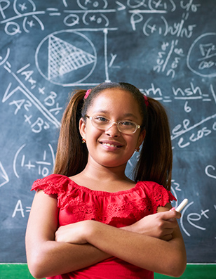 Photo of a young girl in a red shirt standing in front a chalkboard with formulas written on it.